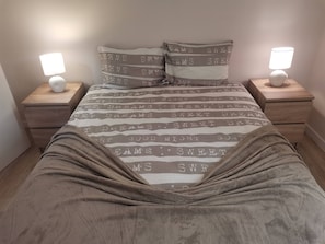 Ein ordentlich gemachtes Bett mit gestreiftem Bettbezug und passenden Kissen, das von zwei Nachttischen mit Lampen gesäumt wird.