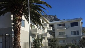 A white car parked in front of a modern apartment building with balconies and a palm tree.