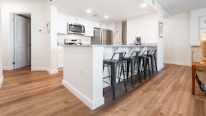 A modern kitchen with white cabinetry, stainless steel appliances, and a bar area with stools. - Sandcastle Condominiums Unit 125  (Port Aransas)