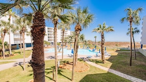 A resort with a pool area, palm trees, and a building with balconies. - Sandcastle Condominiums Unit 125  (Port Aransas)