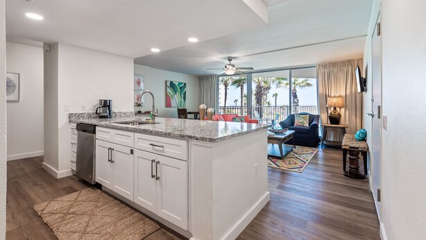 A spacious kitchen with white cabinets, a granite countertop, and a built-in dishwasher. - Sandcastle Condominiums Unit 125  (Port Aransas)