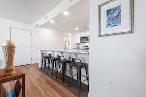 A modern kitchen with a bar area, wooden flooring, and a framed artwork on the wall. - Sandcastle Condominiums Unit 125 (Port Aransas)