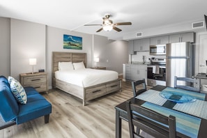 A modern hotel room with a bed, a desk, a dining table, a ceiling fan, and a kitchenette. - Sandcastle Condominiums Unit 207  (Port Aransas)