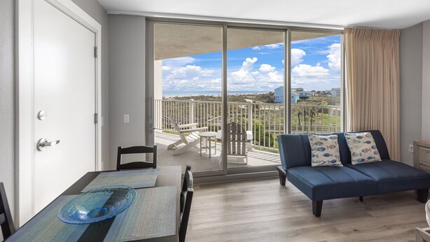 A modern living room with a large sliding glass door leading to a balcony with a view of the beach and houses. - Sandcastle Condominiums Unit 207  (Port Aransas)