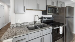 A modern kitchen with granite countertops, stainless steel appliances, and grey cabinetry. - Sandcastle Condominiums Unit 207  (Port Aransas)