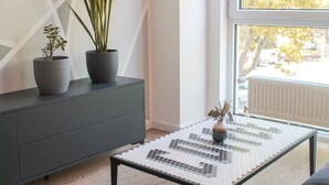 A modern interior with a dark grey cabinet, a glass coffee table with a mosaic pattern, and two potted plants. - New York style, parking lot, lockable bike box with charging facility  (Koblenz)