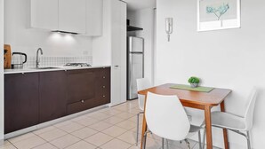 Eine moderne Küche mit weißen Schränken, einem Edelstahlkühlschrank und einem Essbereich mit einem Holztisch und weißen Stühlen.