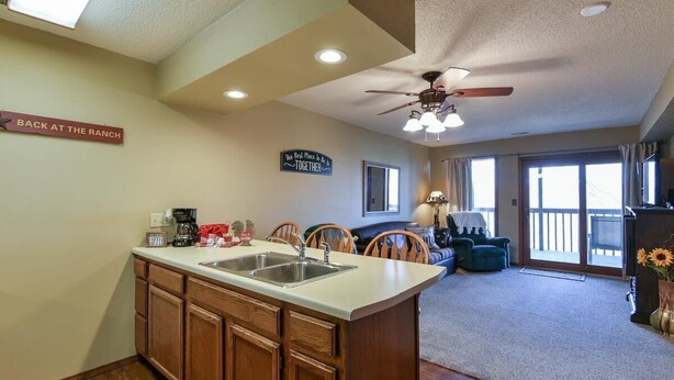 A kitchen with wooden cabinets, a double sink, and a ceiling fan. There is a sign on the wall that reads "Back at the Ranch." - Westcreek Ranch - No Stairs! (Branson West)