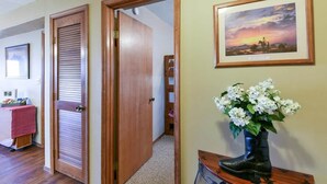 A hallway with wooden doors, a framed painting, and a vase with flowers on a wooden table. - Westcreek Ranch - No Stairs! (Branson West)