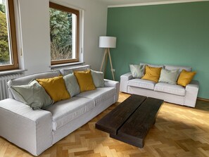 Un salon moderne avec deux canapés gris, un parquet en bois disposé en chevrons, une table basse en bois foncé et un lampadaire.