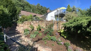 Um jardim com muro de pedra, escadaria e casa com varanda.