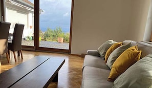 A living room with a sofa, a table, and a view through a glass door to an outdoor area.
