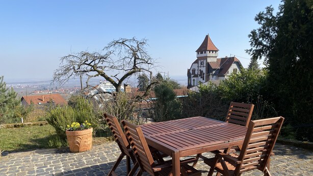 Conjunto de mesa e cadeiras de madeira em um pátio de paralelepípedos, com vista para uma igreja e edifícios ao longe.
