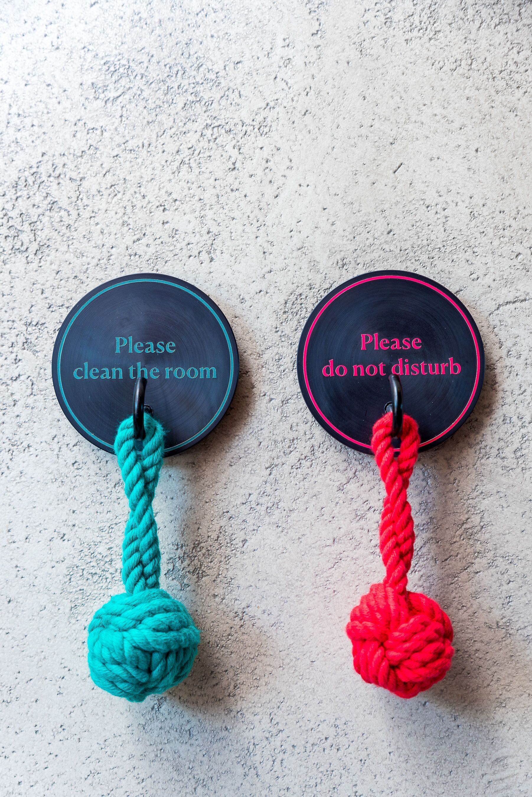 Two wall-mounted signs with ropes, one instructing to clean the room and the other to not disturb.
