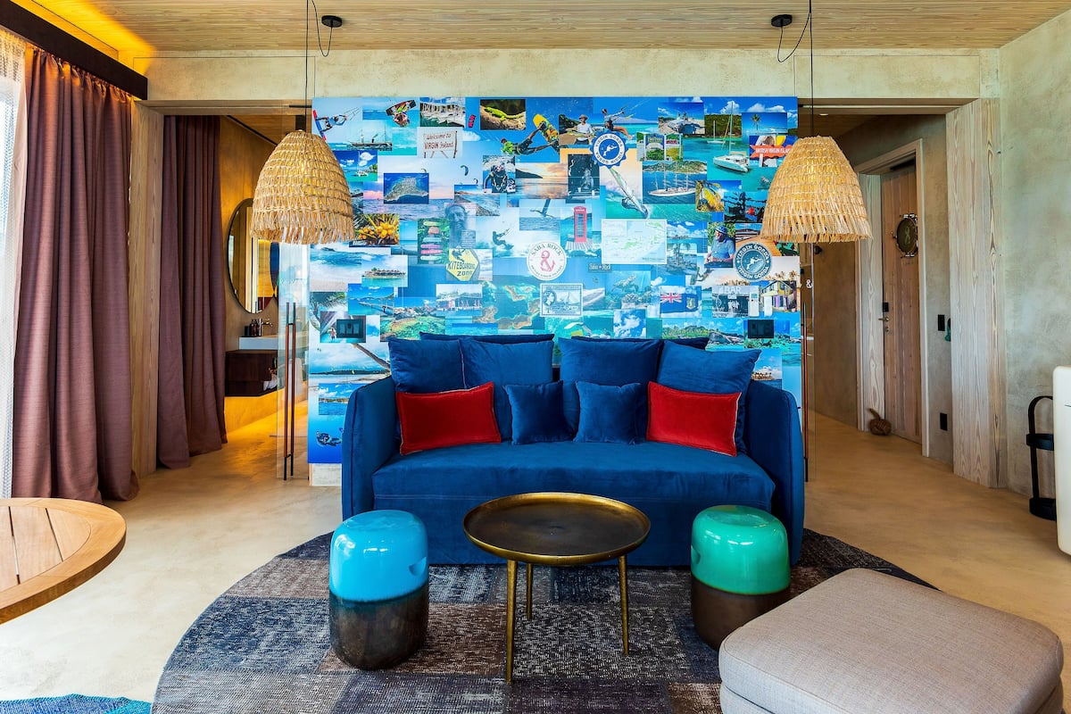 Una sala de estar moderna con un sofá azul, cojines rojos y azules, una mesa de centro redonda y un collage de colores en la pared.