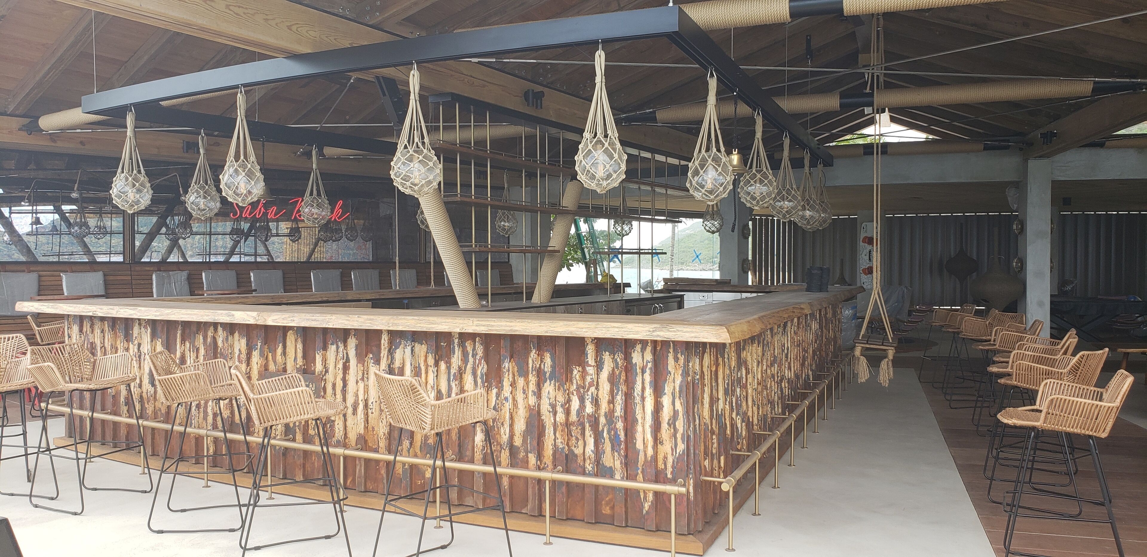 Una zona de bar con un mostrador rústico de madera, lámparas colgantes tejidas y taburetes de mimbre.