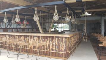 Una zona de bar con un mostrador rústico de madera, lámparas colgantes tejidas y taburetes de mimbre.