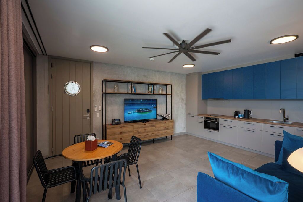 A compact living space with a dining area, a kitchenette, a TV, and a ceiling fan.