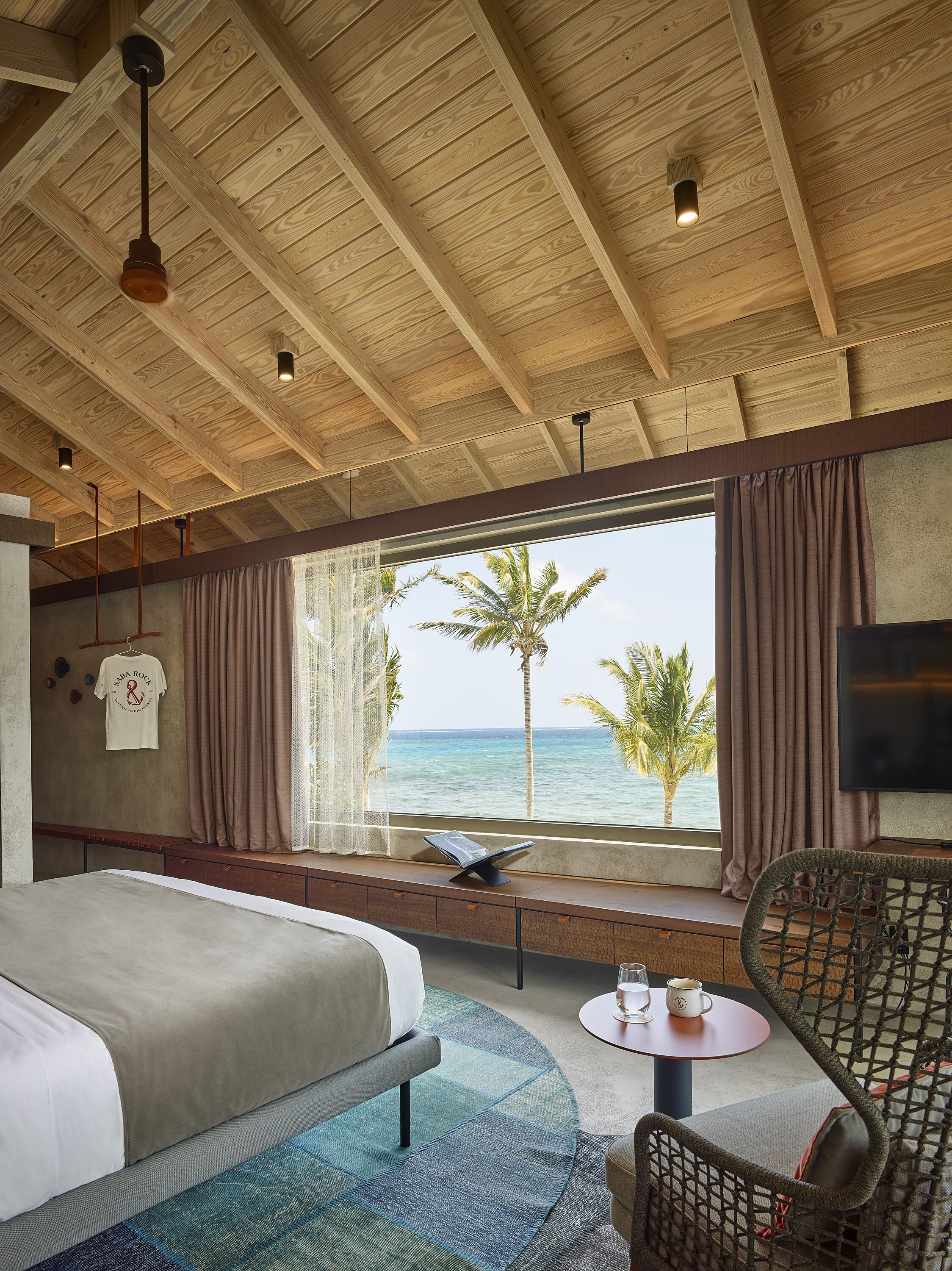 A bedroom with a large bed, a view of the ocean, a window seat, and a TV.