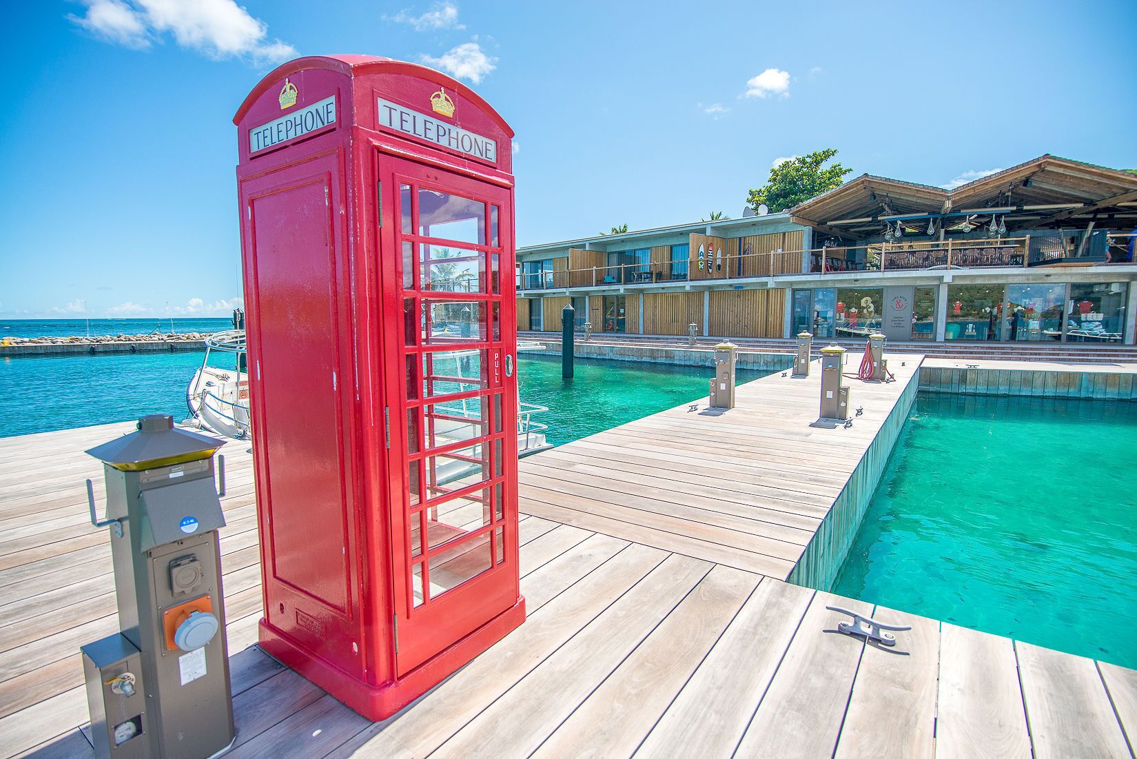 A red telephone booth on a wooden deck by a pool with clear blue water.