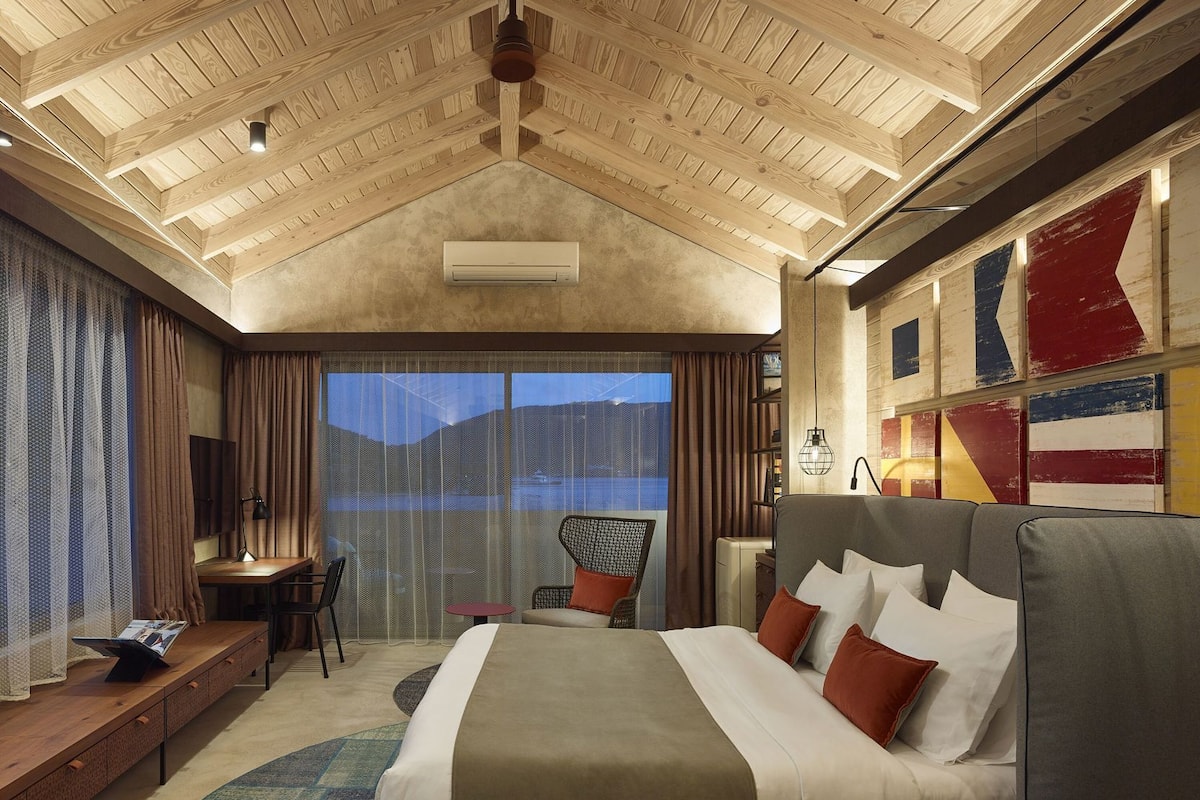 Habitación de hotel con techo de madera, una cama grande, un escritorio y vistas a las montañas.