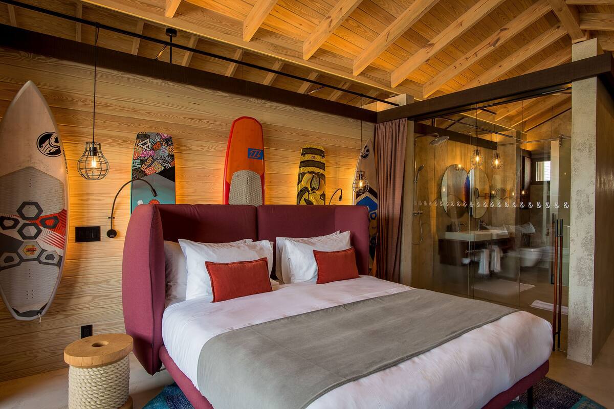 Un dormitorio con techo de madera, una cama con ropa de cama roja y blanca, y tablas de surf en la pared.