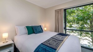 A hotel room with a bed, bedside lamps, and a window with a view of trees.