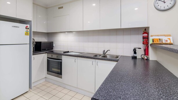 A modern kitchen with white cabinets, a granite countertop, a microwave, a stove, a sink, and a fire extinguisher.