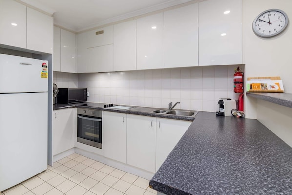A modern kitchen with white cabinets, a granite countertop, a microwave, a stove, a sink, and a fire extinguisher.
