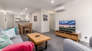 A modern living room with a sofa, a coffee table, a TV, and a dining area with chairs and a table.
