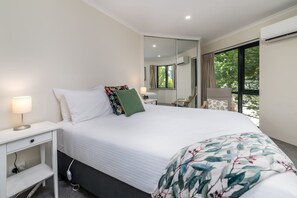 A hotel room with a bed, bedside table, lamp, chair, and a large window with a view of greenery.
