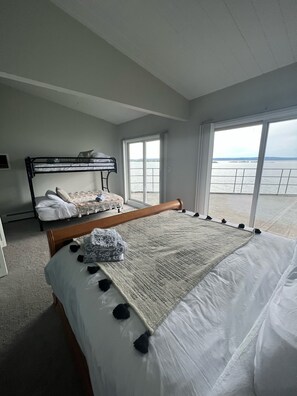 Ein Schlafzimmer mit einem großen Bett, einem Etagenbett und Blick auf das Wasser durch die Fenster.
