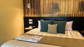 Una cama bien hecha con almohadas, una mesita de noche con un libro y un teléfono, y una pared con listones de madera verticales y una lámpara colgante.