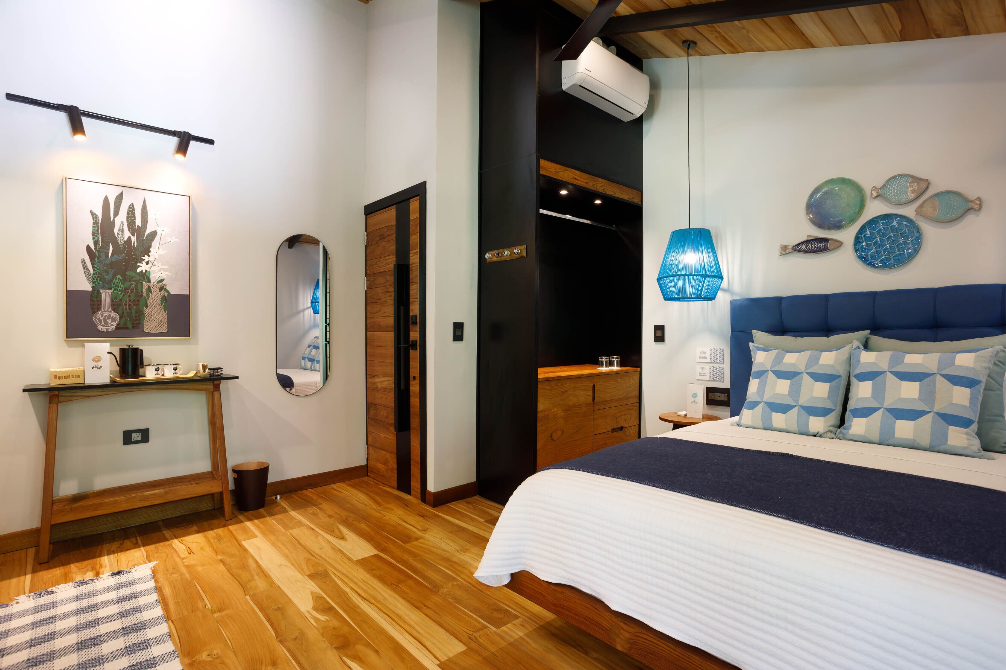 Une chambre à coucher avec un lit, une table de chevet et un miroir. On y trouve également un climatiseur fixé au mur et des assiettes décoratives à motifs de poissons.