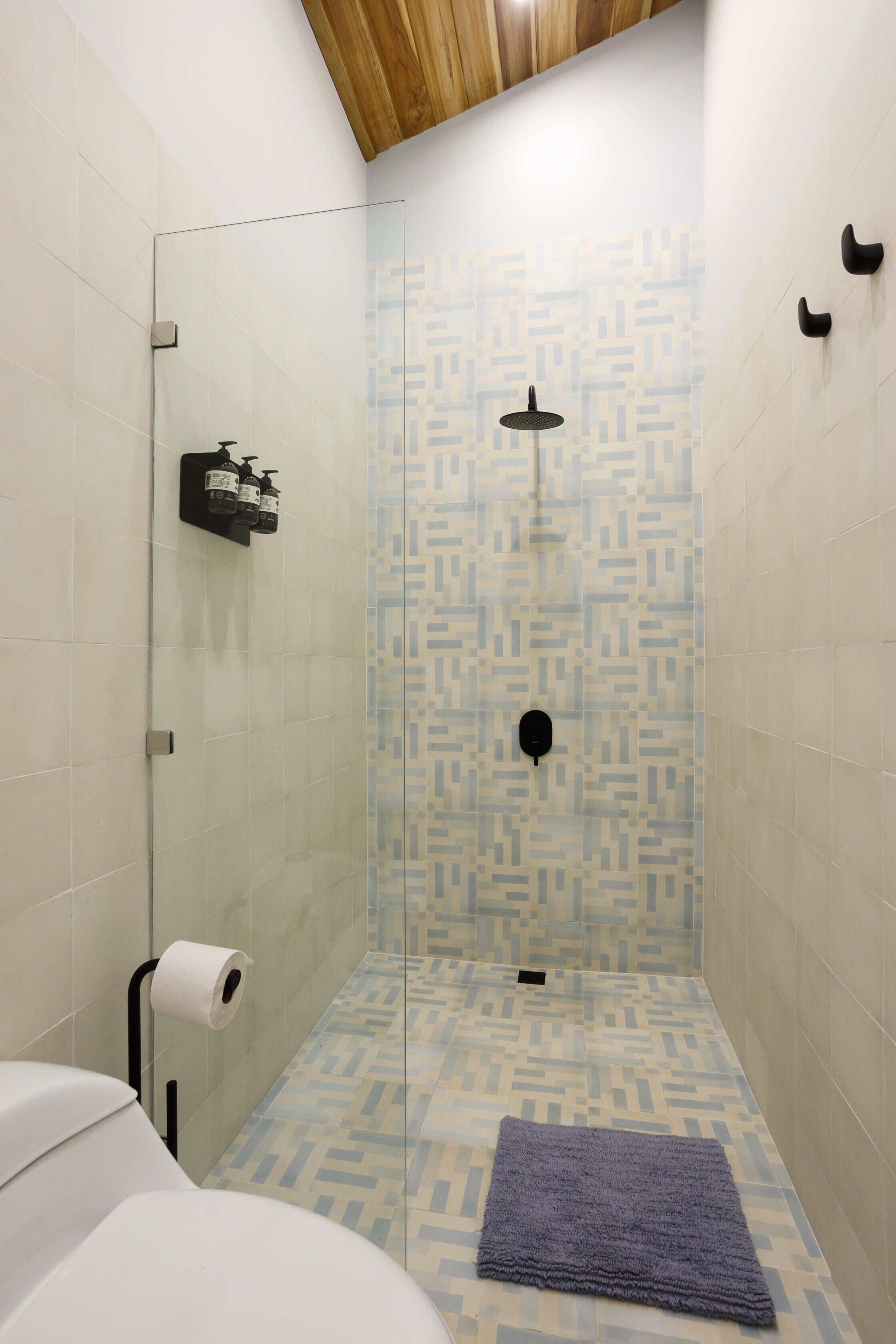 A shower with a patterned tile wall, a glass door, and a wooden ceiling.