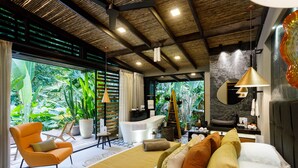 A modern hotel room with a large bed, a sitting area with a chair, a bathtub, and a view of lush greenery. - awā Beachfront Hotel (Cahuita)
