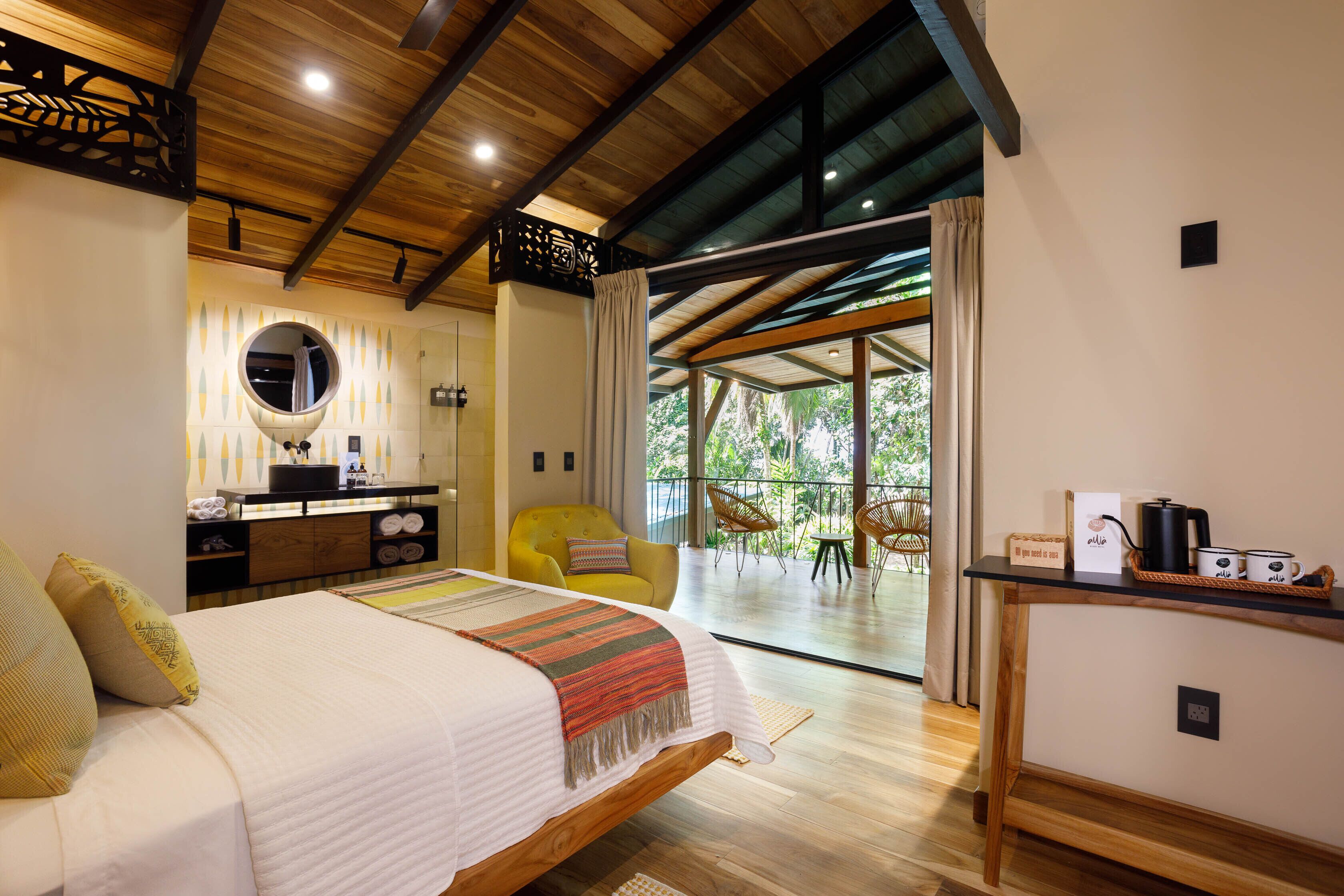Een moderne slaapkamer met een groot bed, een houten plafond, een ronde spiegel, een gele stoel en een balkon met tuinmeubilair.