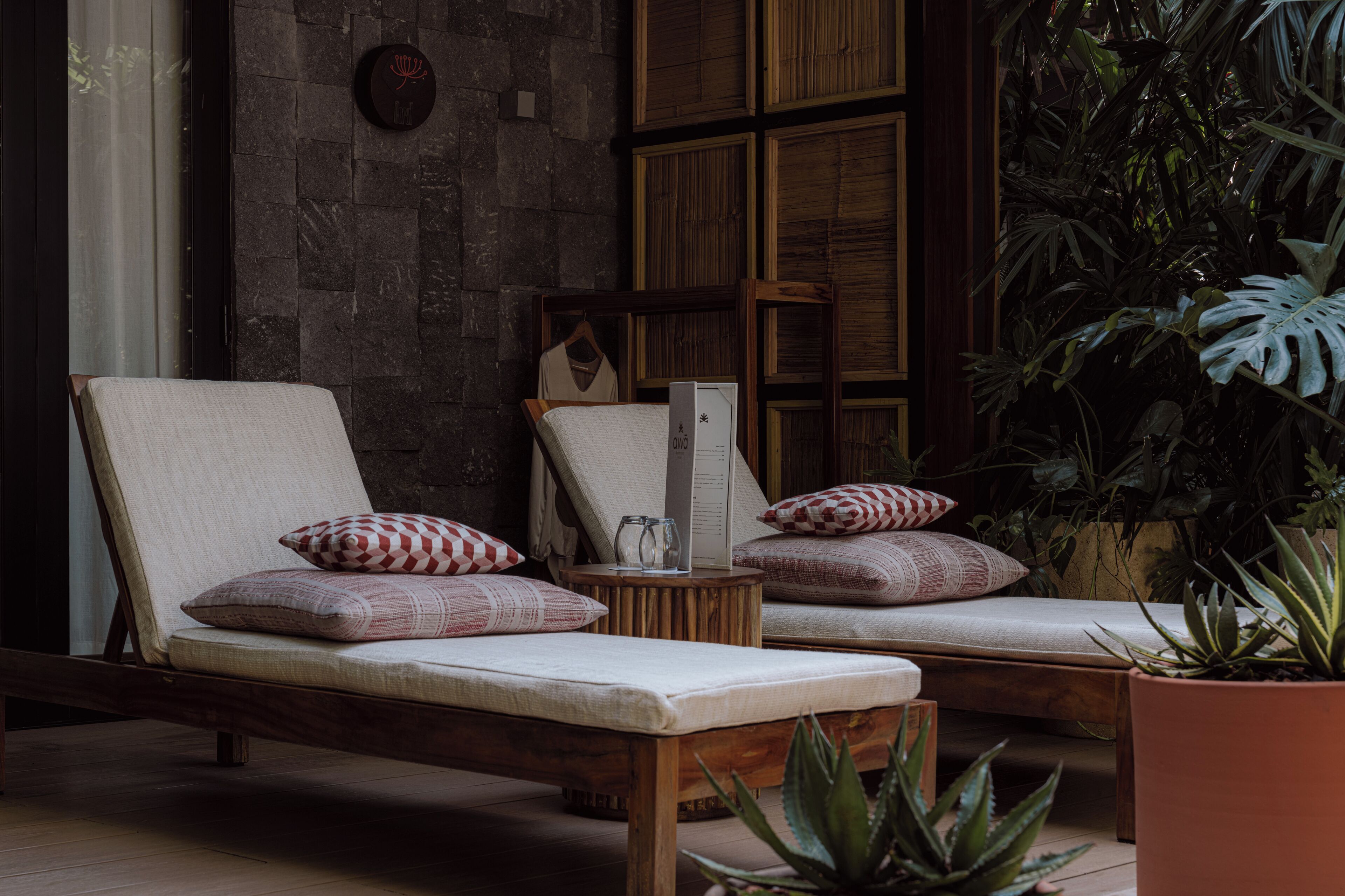 A lounge area with two wooden lounge chairs, each with a cushion and a small table between them.