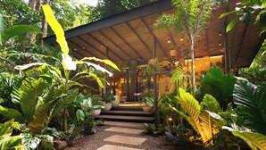 A covered pathway leading to a building with a modern design, surrounded by lush tropical plants. - awā Beachfront Hotel (Cahuita)