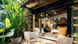 A modern outdoor seating area with wicker furniture, a large potted plant, and a view into a well-lit interior space with a bed and seating area. - awā Beachfront Hotel (Cahuita)