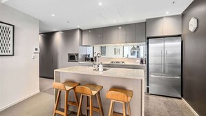 A modern kitchen with a central island, bar stools, stainless steel appliances, and a large refrigerator.