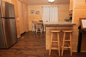 A wooden-paneled kitchen with a stainless steel refrigerator, a wooden dining table with chairs, and a bar area with stools.