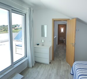 A bedroom with a large window, a wooden door, a bedside table, and a bed with striped bedding.