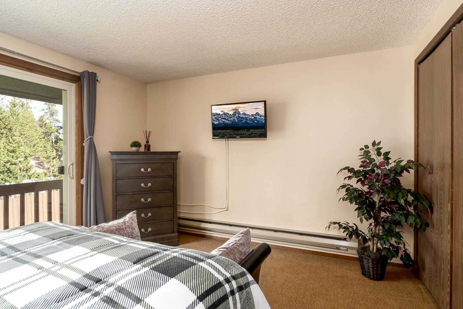 A bedroom with a bed, a dresser, a TV on the wall, and a potted plant.