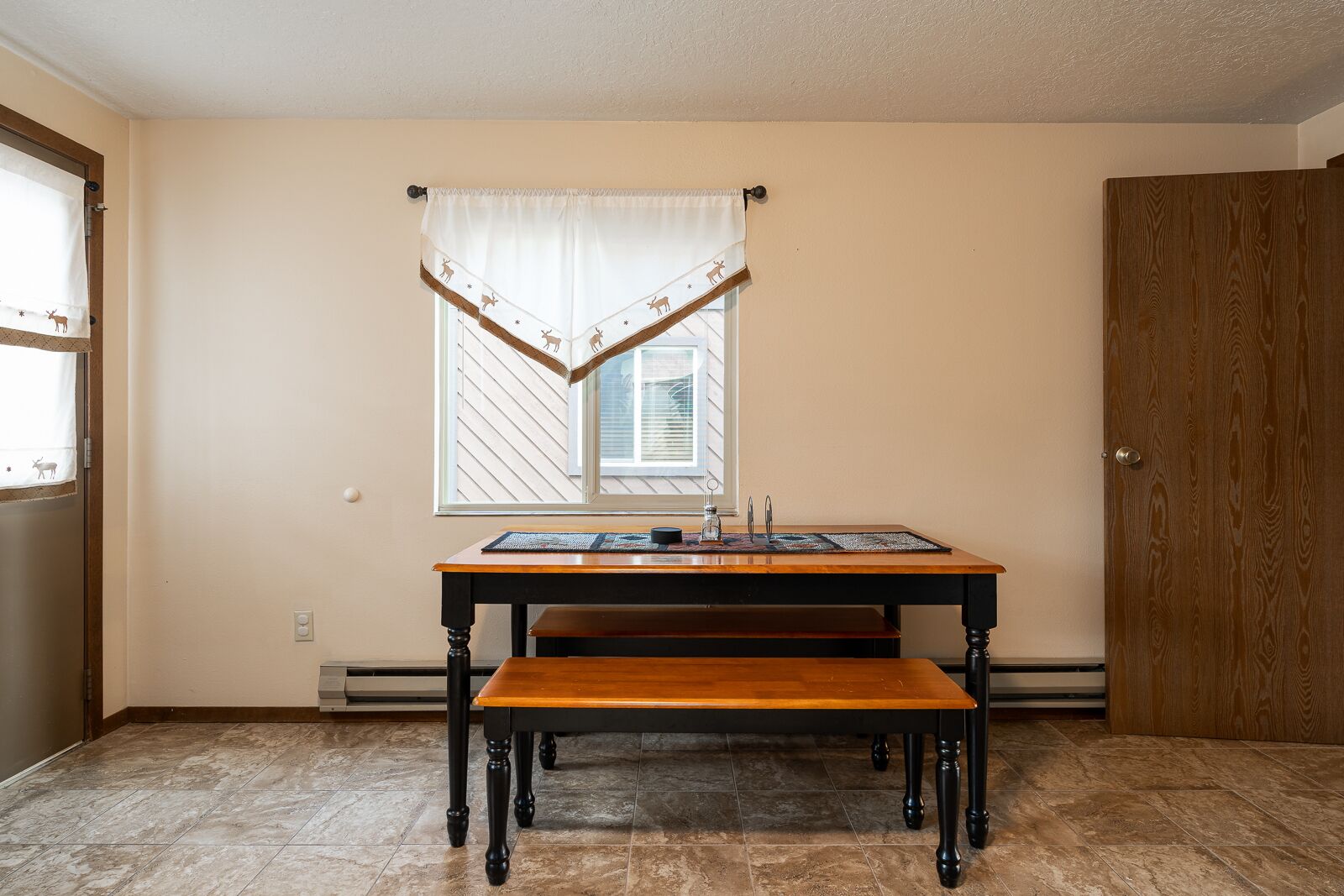 Una habitación con una mesa de madera, un banco, una ventana con persianas y una puerta.