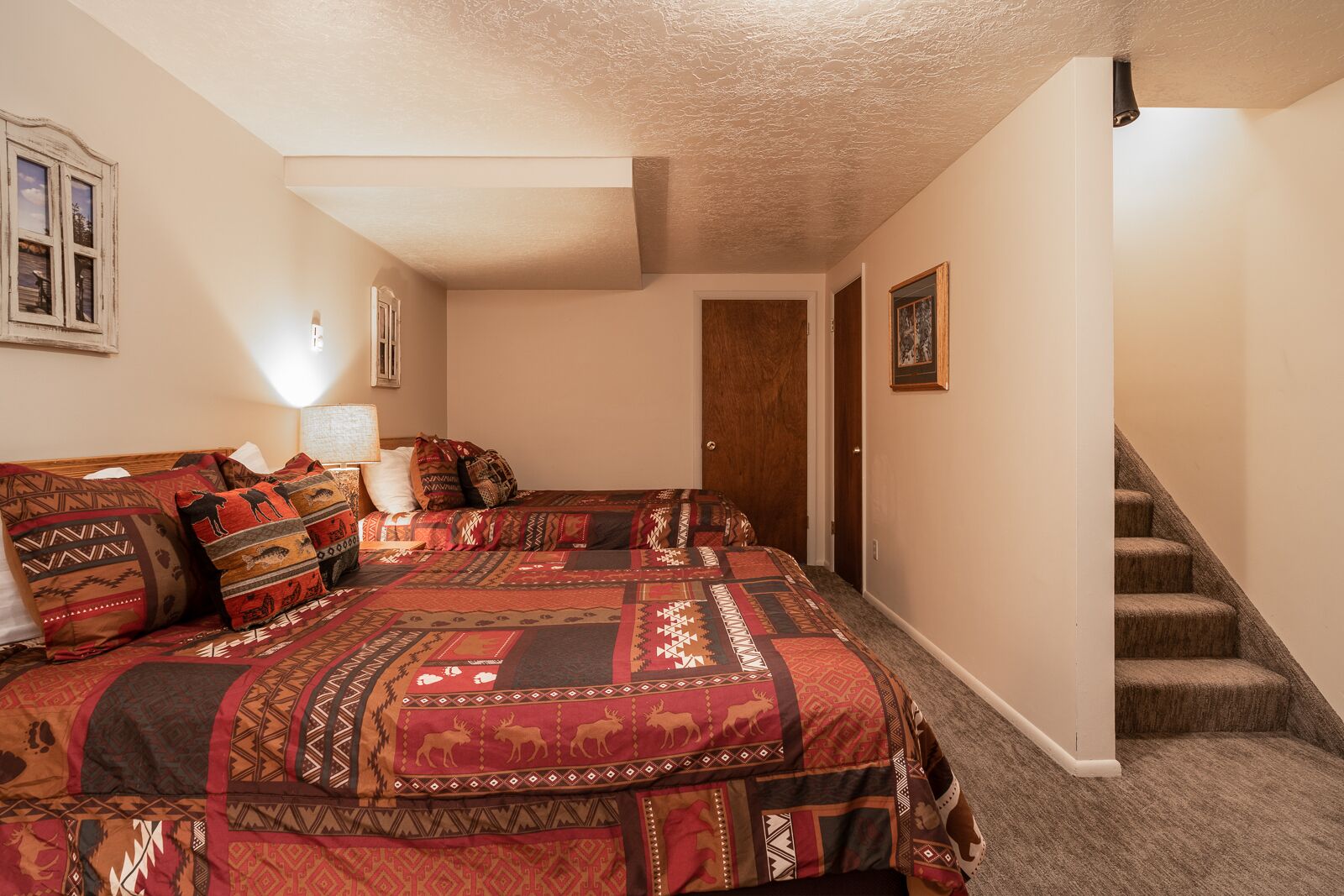 A bedroom with a large bed, a nightstand, a lamp, a wooden door, and a staircase.