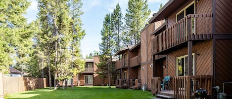 A wooden cabin with a deck, surrounded by tall trees and a well-maintained lawn.
