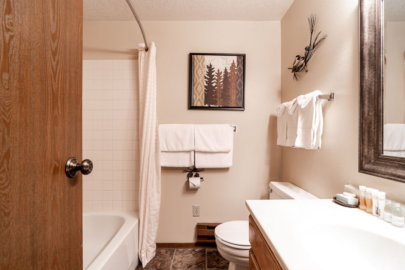 A bathroom with a bathtub, toilet, and sink. There is a framed picture on the wall, a towel rack, and toiletries on the sink.