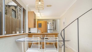 A narrow hallway with a kitchen area featuring a white refrigerator, a wooden cabinet, and a white table with chairs.