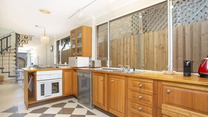 A modern kitchen with wooden cabinets, a built-in dishwasher, and a large window with a view of a wooden fence.